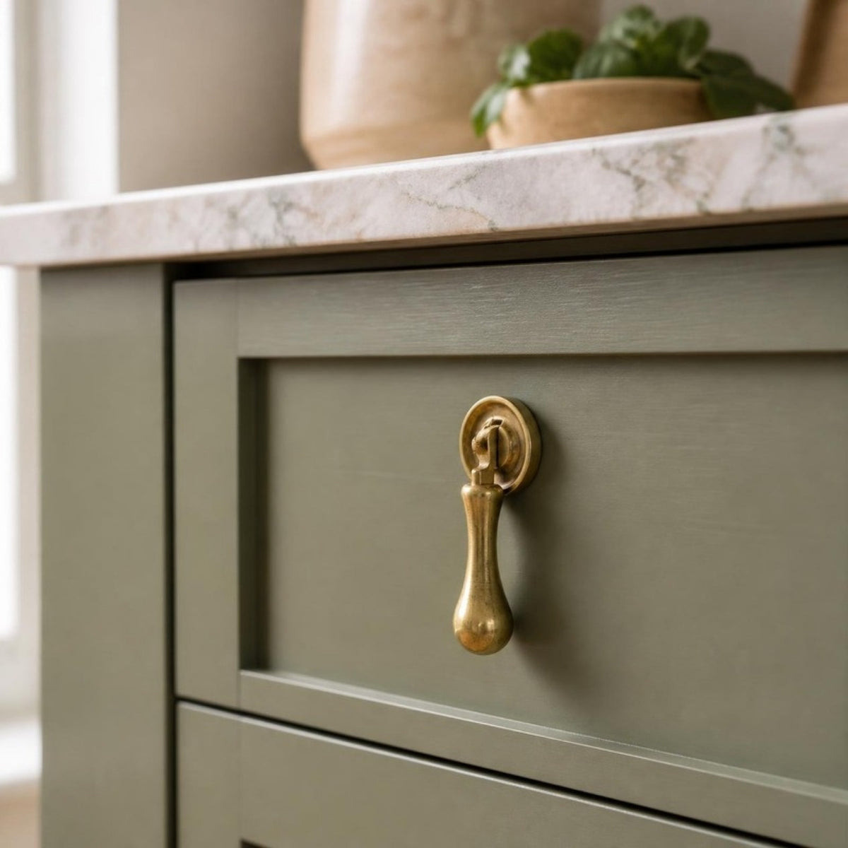 Solid brass tear drop handle on a sage green Shaker kitchen drawer