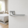 Fedra Italian lever handle on rose on a white timber door ajar to a modern bedroom